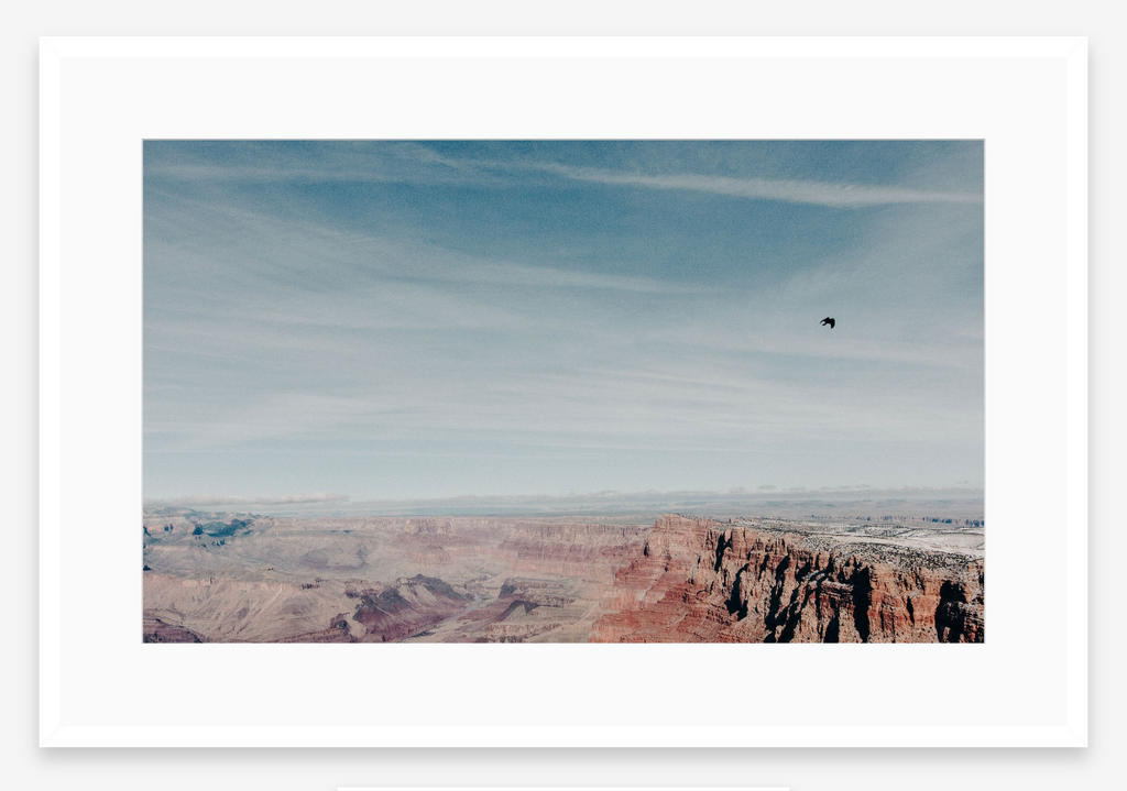 Scenic view of a desert landscape with cliffs and a bird flying in the sky.